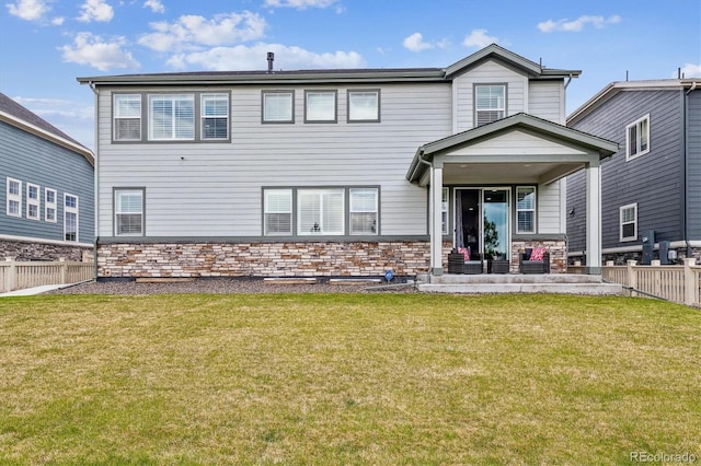 rear view of property featuring stone siding, a lawn, and fence