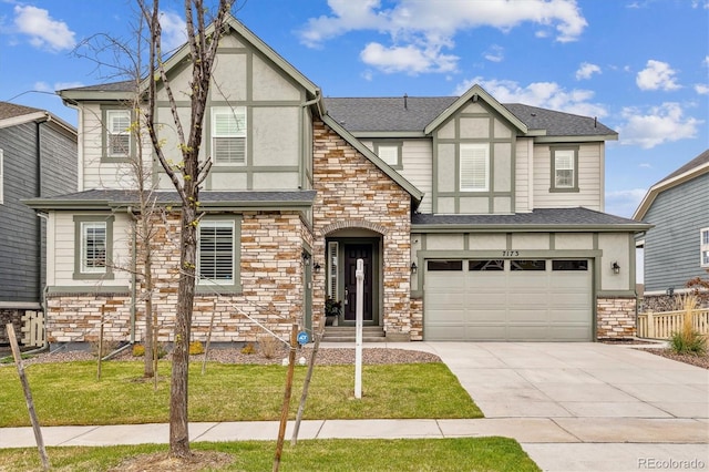 tudor house with concrete driveway, a front yard, stucco siding, stone siding, and an attached garage