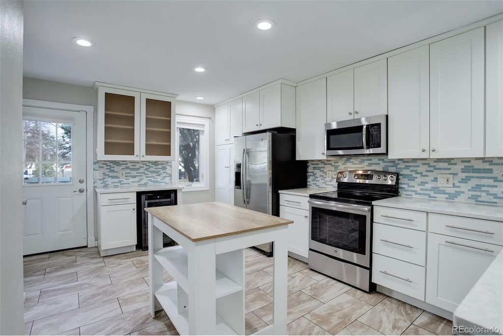 kitchen featuring white cabinets, backsplash, stainless steel appliances, and wine cooler