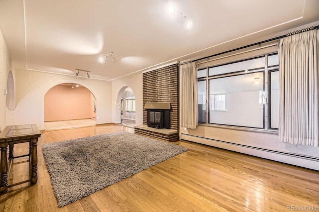 6710 W Nevada Pl, Lakewood, CO 80226 - unfurnished living room featuring arched walkways, track lighting, a baseboard radiator, wood finished floors, and a brick fireplace