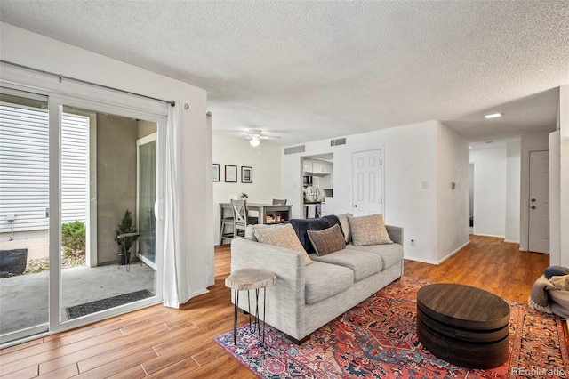 living room with ceiling fan, plenty of natural light, a textured ceiling, and light hardwood / wood-style flooring