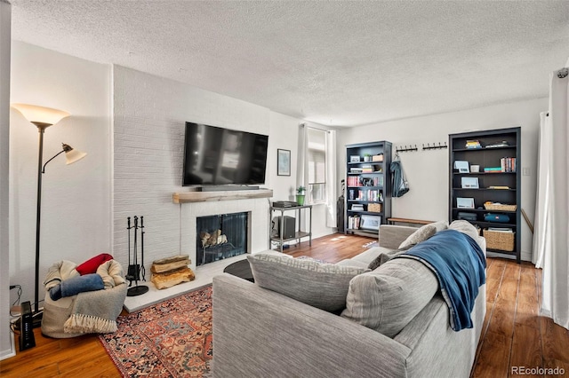 living room with a brick fireplace, a textured ceiling, and hardwood / wood-style floors