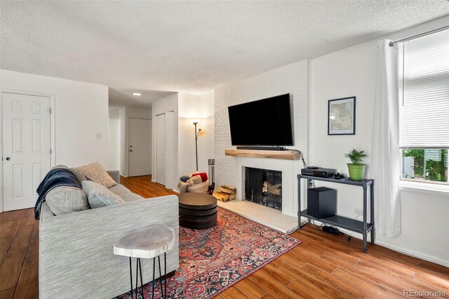 living room featuring a brick fireplace, wood-type flooring, and a textured ceiling