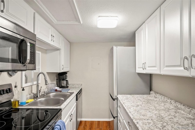 kitchen with appliances with stainless steel finishes, a textured ceiling, white cabinets, and light wood-type flooring