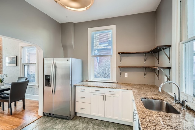 kitchen with stainless steel refrigerator with ice dispenser, light stone countertops, sink, and white cabinets