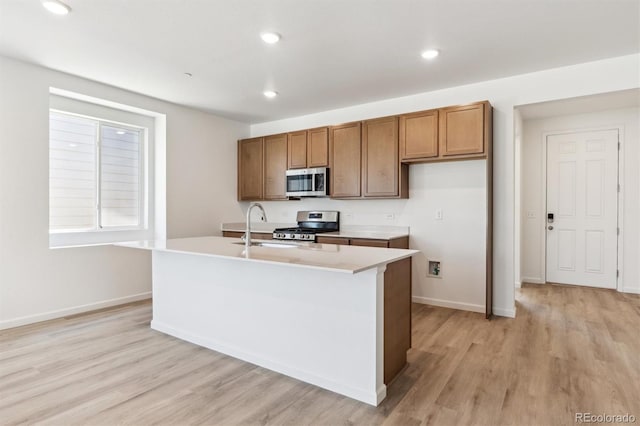 18951 E 96th Pl, Commerce City, CO 80022 - kitchen with stainless steel appliances, brown cabinetry, light wood-style flooring, a kitchen island with sink, and recessed lighting