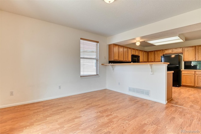 5831 Moon Ridge Dr, Colorado Springs, CO 80922 - kitchen with black appliances, light wood-style flooring, a kitchen breakfast bar, a peninsula, and baseboards