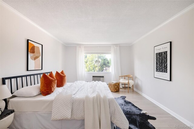 bedroom featuring a wall unit AC, crown molding, light hardwood / wood-style floors, a textured ceiling, and a fireplace