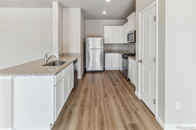 kitchen with light stone counters, a peninsula, stainless steel appliances, light wood-type flooring, and a sink