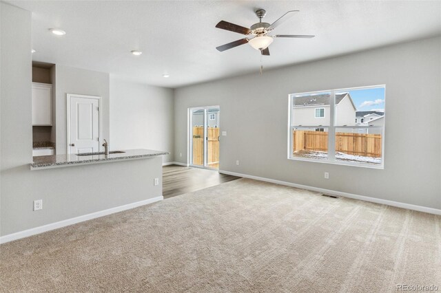 unfurnished living room featuring a sink, baseboards, visible vents, and carpet flooring