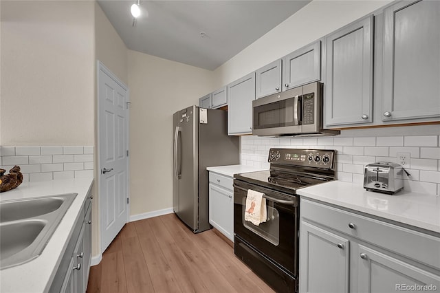 kitchen with light wood-style floors, appliances with stainless steel finishes, a sink, and gray cabinetry