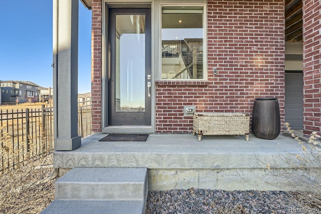 doorway to property featuring fence and brick siding