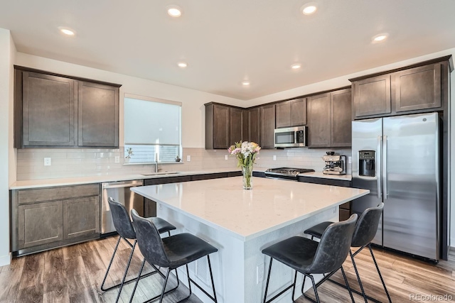 kitchen featuring stainless steel appliances, a sink, dark brown cabinets, and a kitchen bar