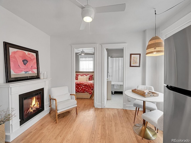 sitting room featuring ceiling fan, light wood-style flooring, a glass covered fireplace, and baseboards