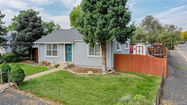 view of front of property with a front lawn, a shingled roof, fence, and stucco siding