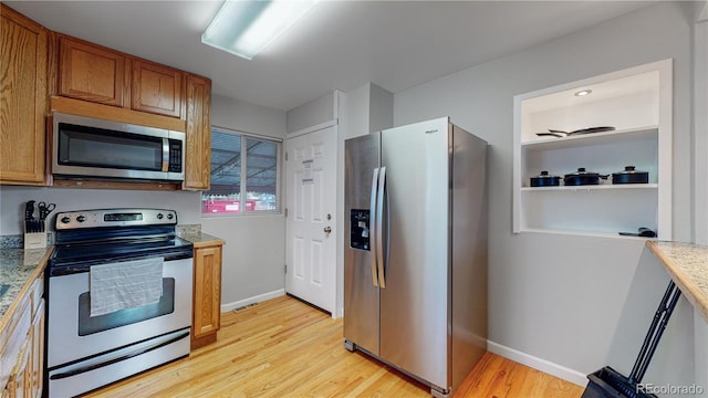 kitchen with appliances with stainless steel finishes, light wood-type flooring, brown cabinetry, and baseboards