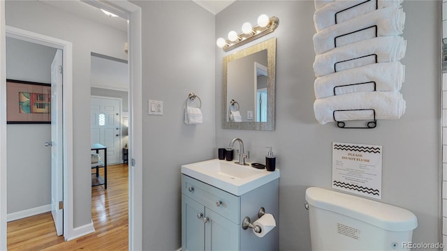 half bath with baseboards, vanity, toilet, and wood finished floors