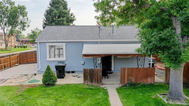 rear view of property with a shingled roof, a patio area, fence, and a lawn