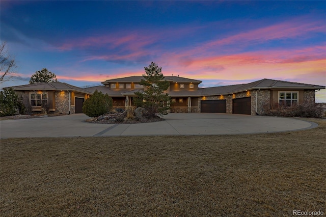 prairie-style home featuring a garage, concrete driveway, stone siding, and a front yard