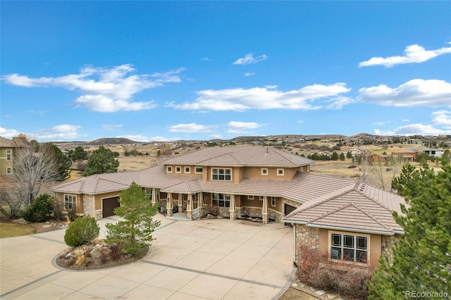 prairie-style home with a mountain view, stone siding, concrete driveway, a tiled roof, and stucco siding