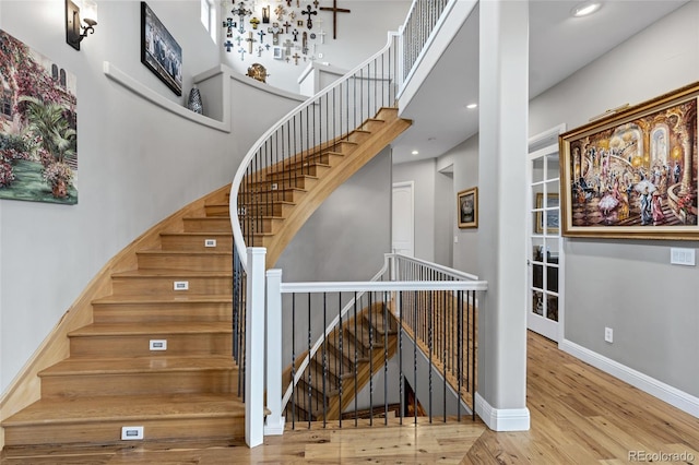 stairway with a high ceiling, recessed lighting, wood finished floors, and baseboards