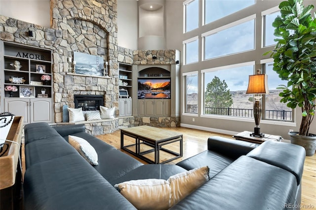 living room with a fireplace, a towering ceiling, baseboards, and wood finished floors