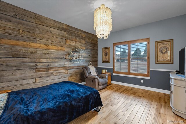 bedroom featuring wooden walls, baseboards, an accent wall, wood finished floors, and an inviting chandelier