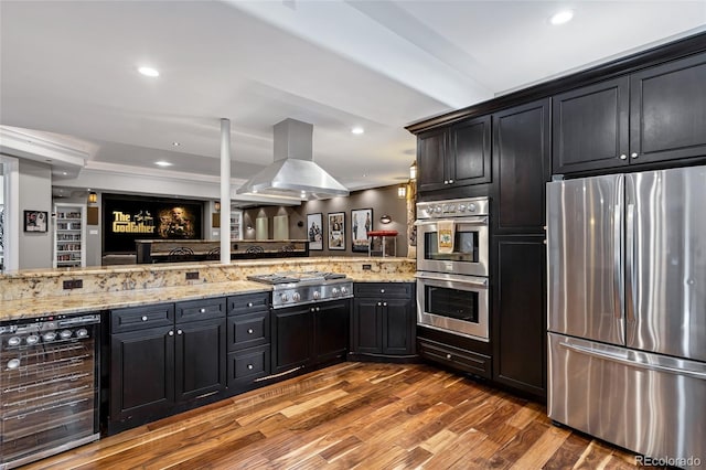 kitchen with beverage cooler, appliances with stainless steel finishes, light stone counters, wood finished floors, and island exhaust hood