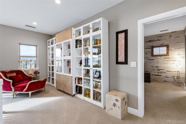 sitting room with wood walls, visible vents, a wealth of natural light, and carpet flooring