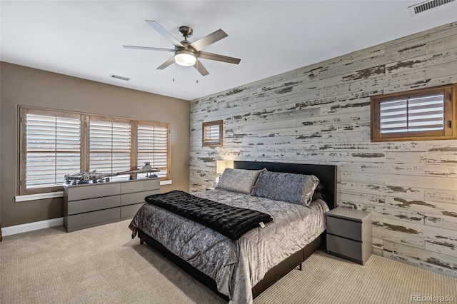 carpeted bedroom featuring visible vents, ceiling fan, wood walls, and baseboards