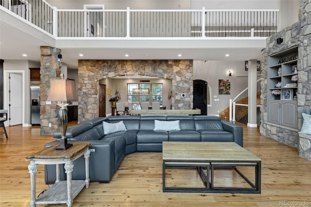 living area featuring arched walkways, a fireplace, a towering ceiling, stairway, and light wood finished floors