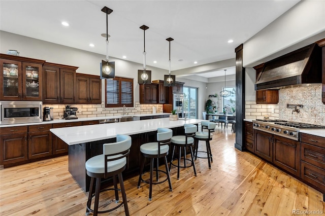 kitchen featuring stainless steel appliances, light countertops, light wood-style floors, dark brown cabinets, and wall chimney exhaust hood