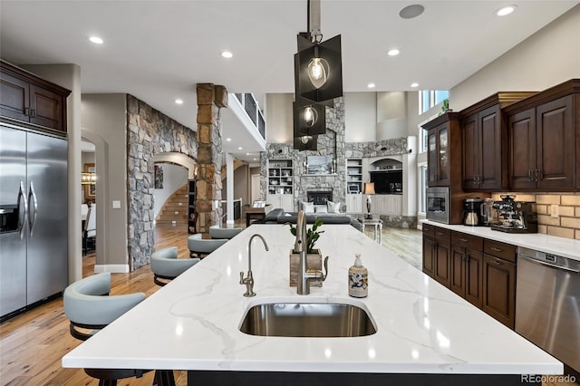 kitchen featuring a kitchen island with sink, appliances with stainless steel finishes, dark brown cabinets, and a stone fireplace