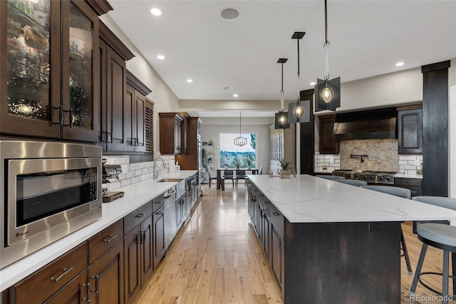 kitchen featuring glass insert cabinets, stainless steel microwave, light stone counters, ventilation hood, and light wood-style floors