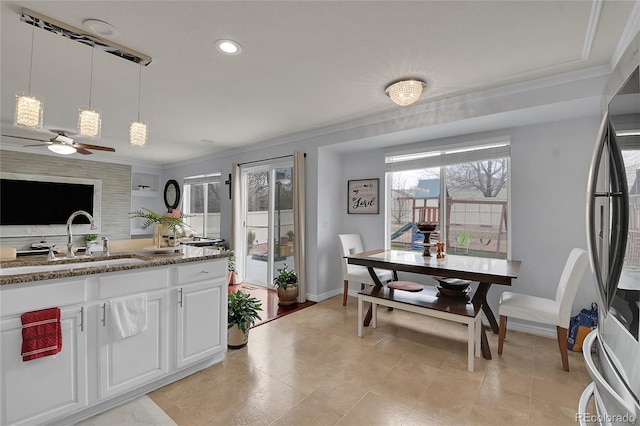 kitchen with white cabinetry, sink, ceiling fan, stainless steel fridge, and decorative light fixtures