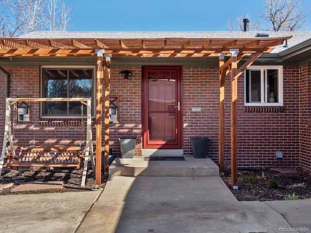 doorway to property featuring brick siding and a pergola