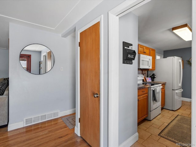 kitchen with dark countertops, visible vents, white appliances, and baseboards