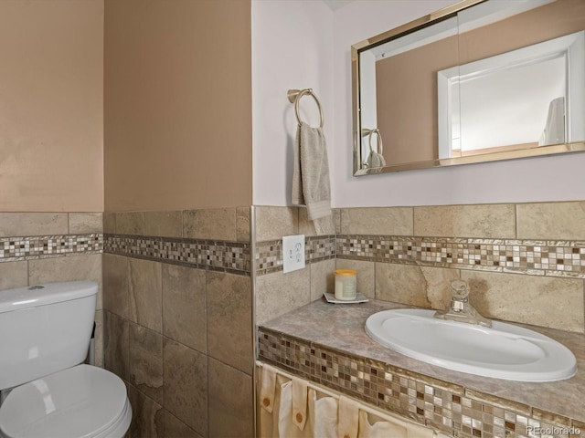 bathroom with tile walls, toilet, a wainscoted wall, and a sink