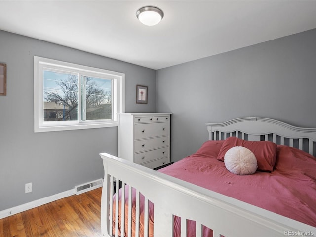 bedroom with wood finished floors, visible vents, and baseboards