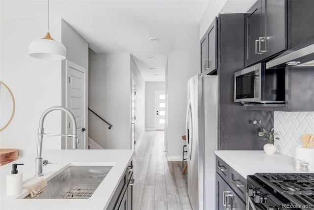 kitchen featuring tasteful backsplash, sink, hanging light fixtures, stainless steel appliances, and light wood-type flooring