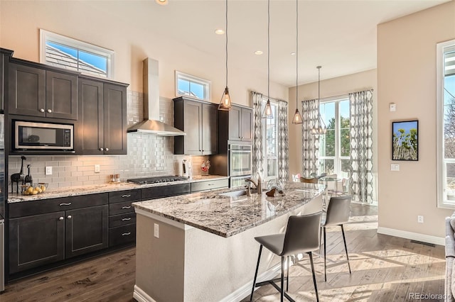 12114 Alcott St, Westminster, CO 80234 - kitchen with appliances with stainless steel finishes, wall chimney exhaust hood, baseboards, decorative backsplash, and light stone counters