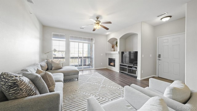 living room with dark wood-type flooring, ceiling fan, and a tiled fireplace