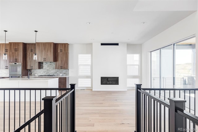 kitchen with light wood-type flooring, plenty of natural light, hanging light fixtures, and backsplash