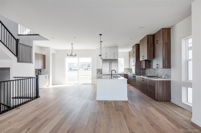 kitchen with a kitchen island with sink, an inviting chandelier, light hardwood / wood-style flooring, stainless steel gas stovetop, and hanging light fixtures