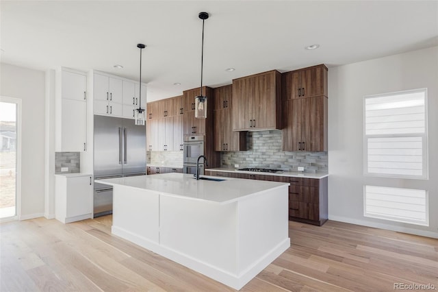 kitchen with an island with sink, hanging light fixtures, stainless steel appliances, and light hardwood / wood-style flooring