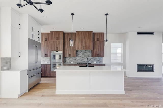 kitchen featuring a center island with sink, pendant lighting, stainless steel appliances, and light wood-type flooring