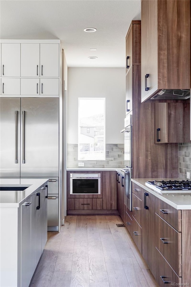 kitchen with decorative backsplash, light wood-type flooring, stainless steel appliances, white cabinets, and exhaust hood