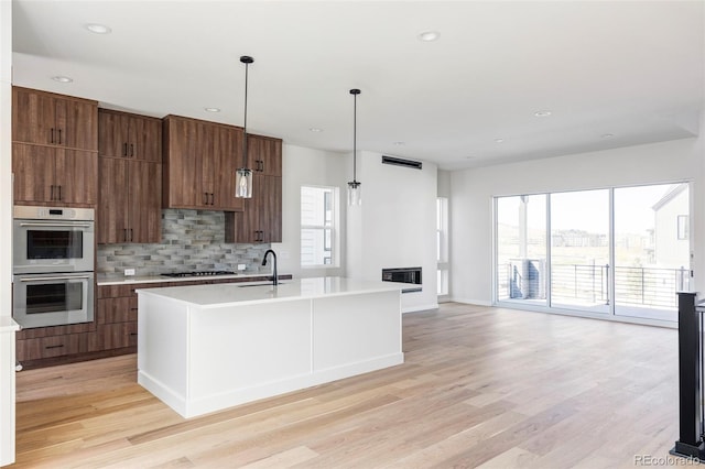 kitchen featuring a kitchen island with sink, light wood-type flooring, stainless steel appliances, and a healthy amount of sunlight