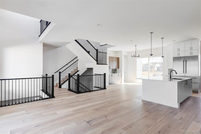 kitchen with hanging light fixtures, sink, a center island with sink, white cabinetry, and light hardwood / wood-style floors