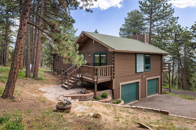 153 Divide View Dr, Golden, CO 80403 - view of front facade with driveway, an attached garage, a chimney, a wooden deck, and roof with shingles